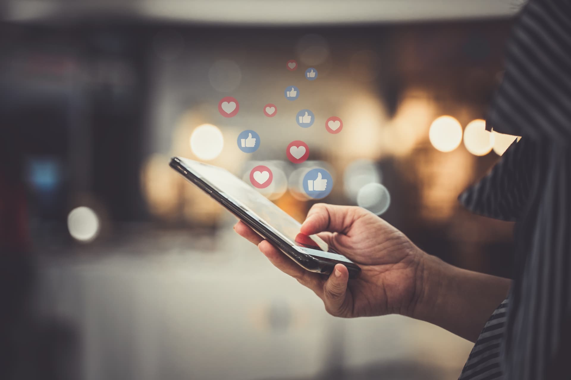 Hand holding a phone with social likes and hearts floating above it